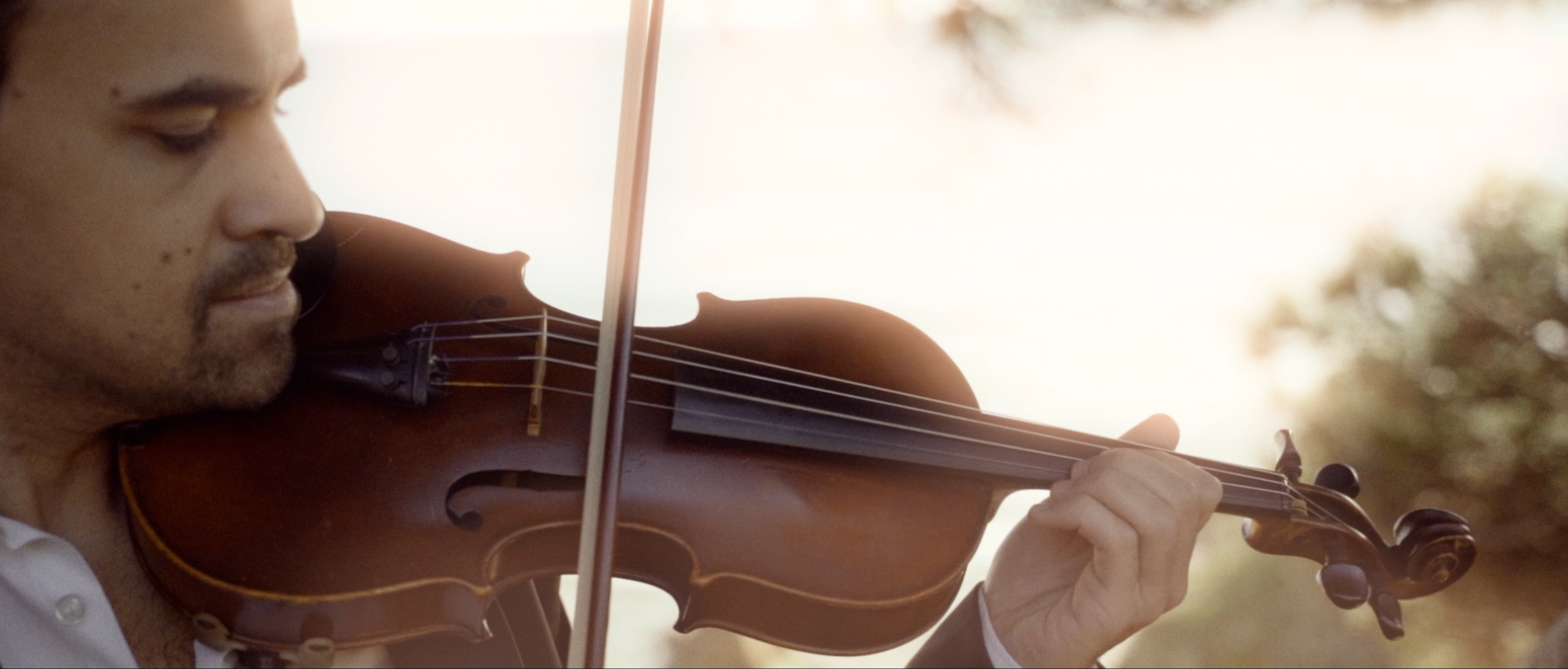 Cinematic close-up of E. Sousa playing violin with a tree in the background